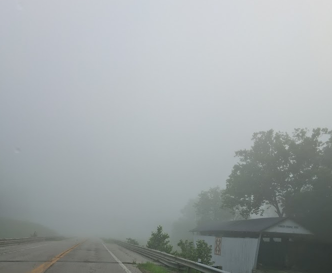 Roadway with heavy fog. A covered, wood bridge to the right.