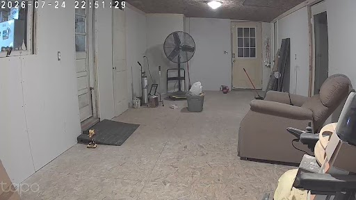a large room, interior, door ahead, on right and on left. Drywall and wooden floor. A recliner in the foreground